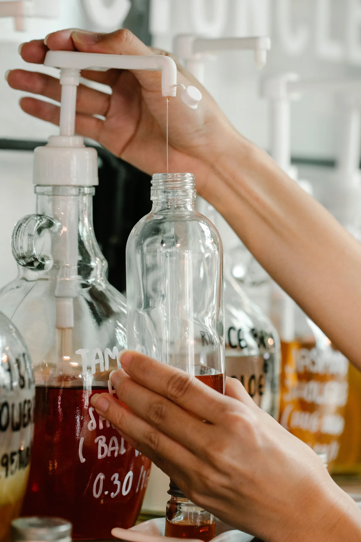 Anonymous hands holding a clear bottle under a liquid dispenser.