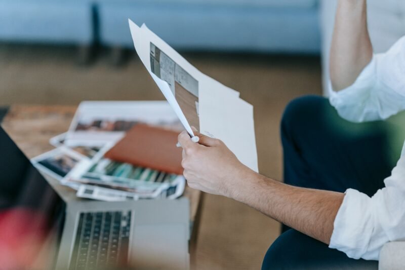 Close-up of a person reviewing papers beside a laptop at home.