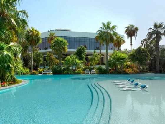 Curving turquoise pool with submerged loungers, palm trees and the glass-fronted Bay Health Club beyond.