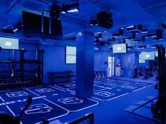 Blue-lit Hero’s Journey training space with dumbbells, exercise bikes and marked stations.