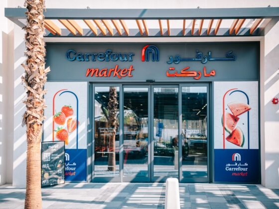 The entrance to a Carrefour Market, framed by palm trees and a shaded pergola