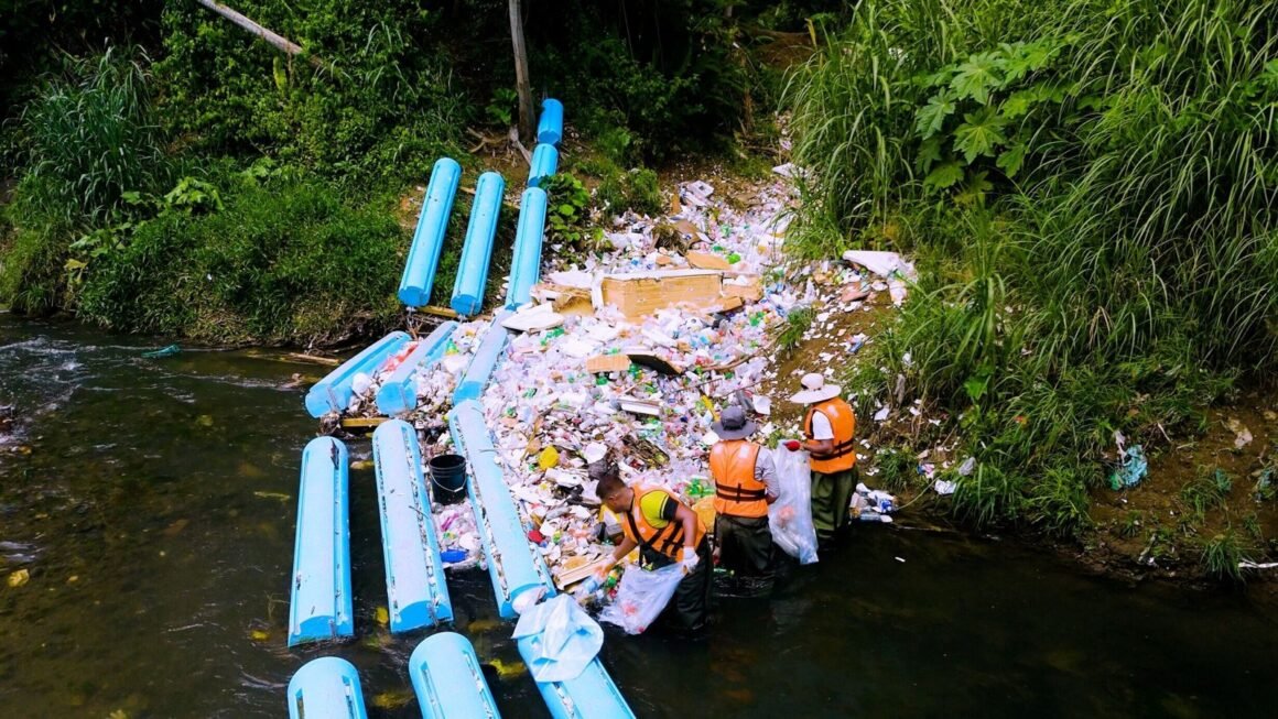 Workers remove captured material beside a river interception barrier in the supplied Panama City project photographs.