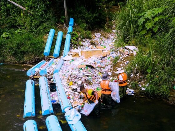 Workers remove captured material beside a river interception barrier in the supplied Panama City project photographs.