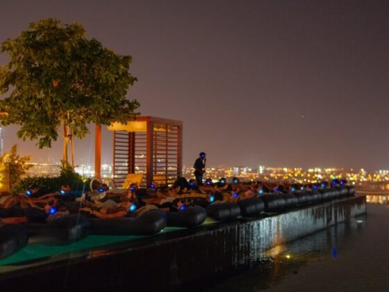 Participants wearing headphones on floating mattresses at a nighttime rooftop pool session.