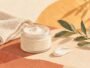 An unbranded moisturiser jar and a folded towel in a warm editorial illustration.