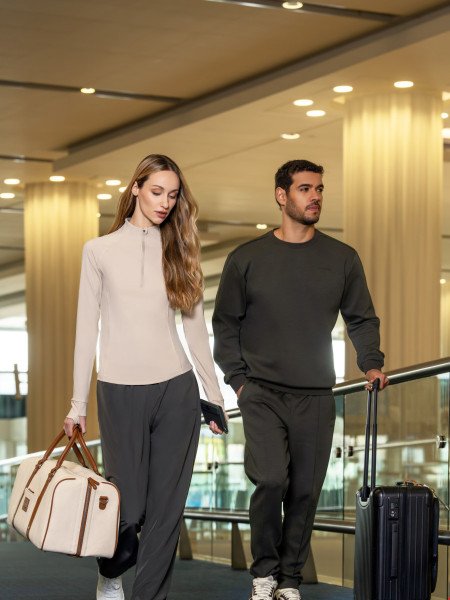 Two models in relaxed travel separates walking through an airport terminal with luggage.