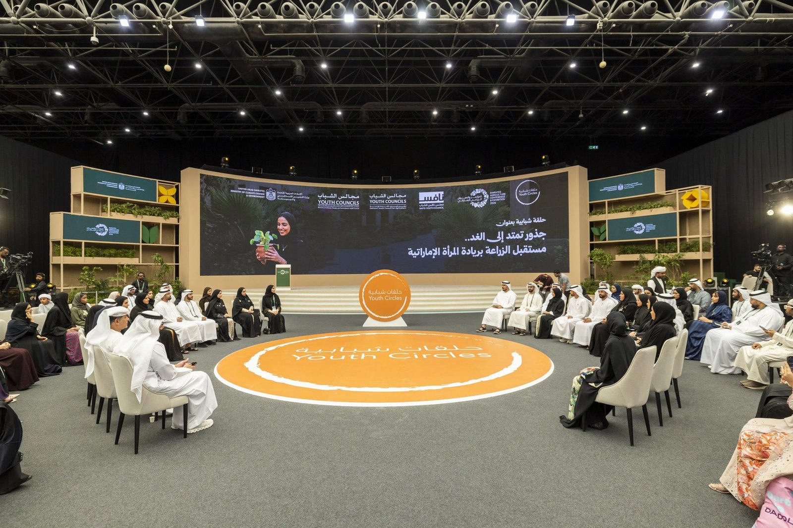 Participants seated in a circle at an agricultural discussion, with a speaker on a large screen