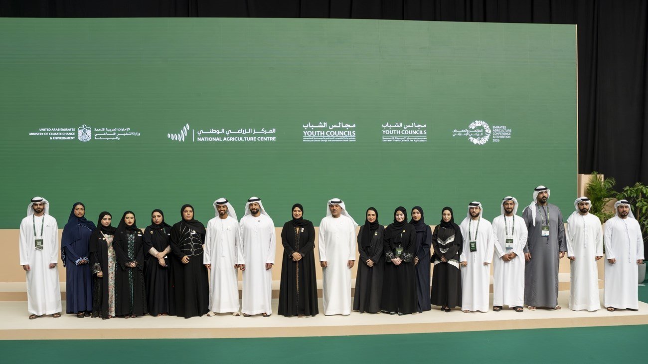 A group of agricultural programme participants standing on a stage before a green backdrop